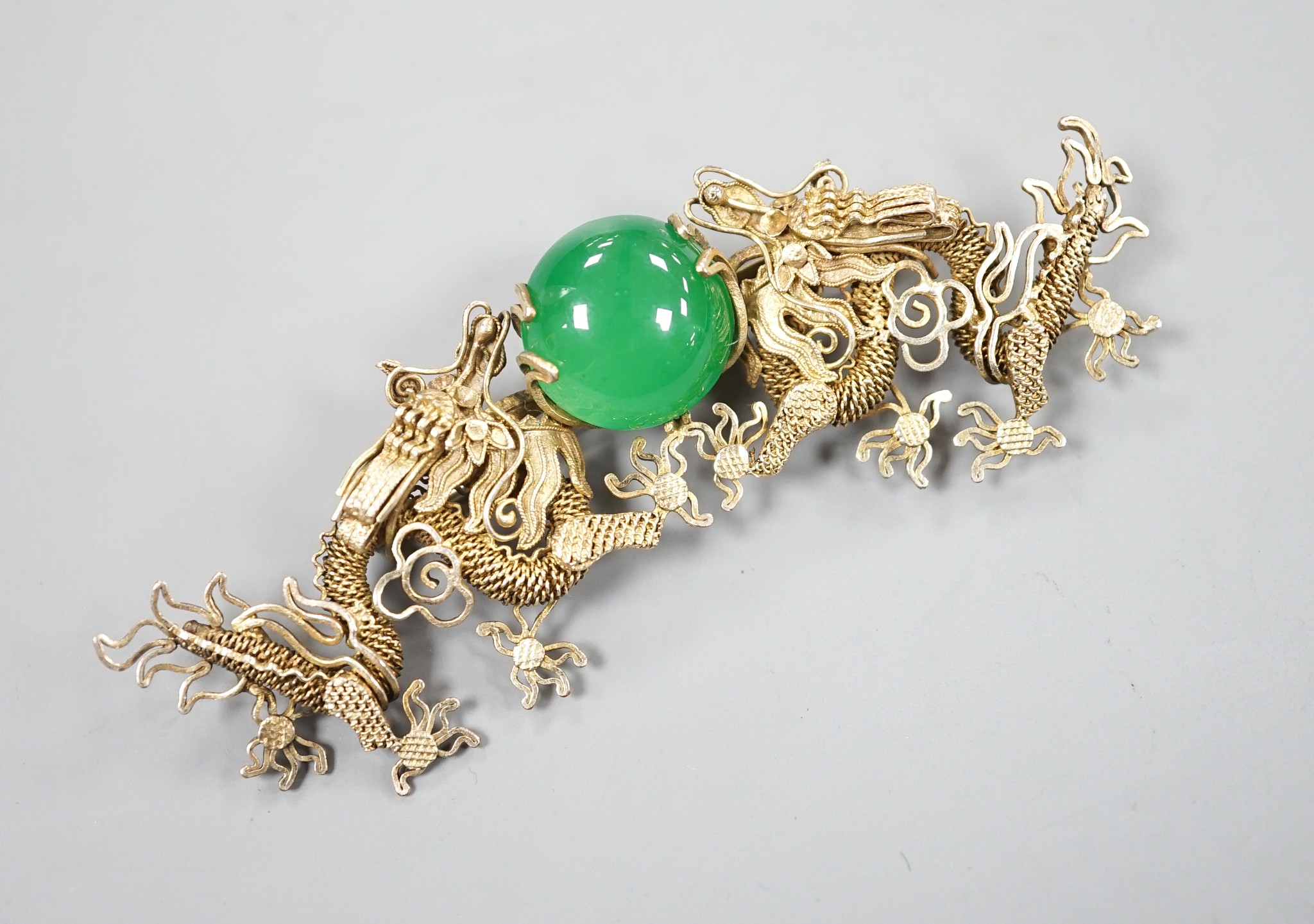 A Chinese gilt white metal and green cabochon stone set filigree dragon brooch, 88mm.